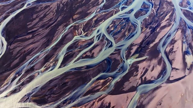 An abstract nature shot featuring the majestic flow of glacial meltwater traversing a volcanic delta in Iceland. The vivid colors of the water stand out brilliantly against the dark sands.