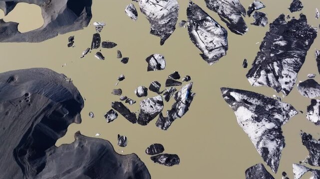 Aerial overview of dark volcanic icebergs floating in an Iceland glacier lagoon, drone backdrdop of meltwater and brownish tinge at surface