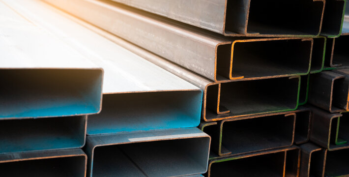 Industrial warehouse stock of rectangular metal pipes for building and construction supplies. Stack of steel pipes. Iron materials for construction and infrastructure projects. Steel tubing storage.