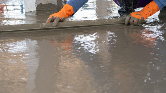 Mason worker working with trowel to level cement floor at construction site. A skilled construction worker spreading wet concrete to level wet concrete on a site floor. Foundation and flooring tasks.