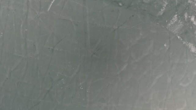 In Brzączowice, Poland, the frozen surface of Lake Dobczyce displays cracked ice patterns across a winter landscape, viewed from an aerial perspective on a sunny day.