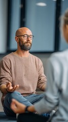 Fototapeta premium Calm bearded man practicing mindfulness meditation in a modern indoor setting, focusing on relaxation and inner peace. He sits cross legged with closed eyes, embracing tranquility