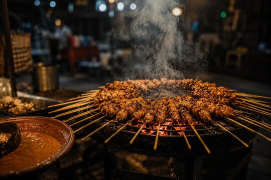 Smoking Chicken Satay Skewers Grilling on Round Charcoal Grill with Peanut Sauce, Indonesia Street Food
