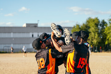 Fototapeta premium Young baseball players huddling together and lifting a teammate in the air, celebrating a win on the field