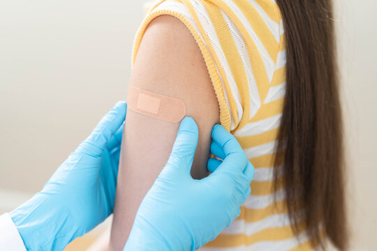 Close up of doctor applying adhesive bandage on girl arm after vaccination.