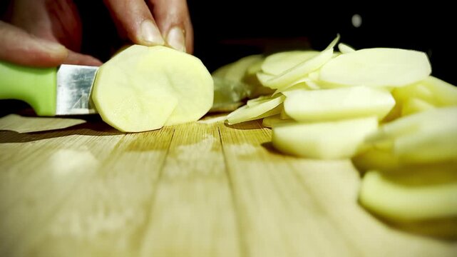 Close-up of chef hands slicing raw potato into thin rounds on a wooden board