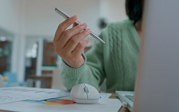 Close up of businesswoman spinning pen and working from home on laptop.