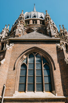 Low angle view of ornate brick church facade, vaulted arch window and spire against clear blue sky above
