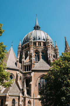 Historic cathedral facade with dome, spires, arched windows and leafy trees beneath clear blue sky day
