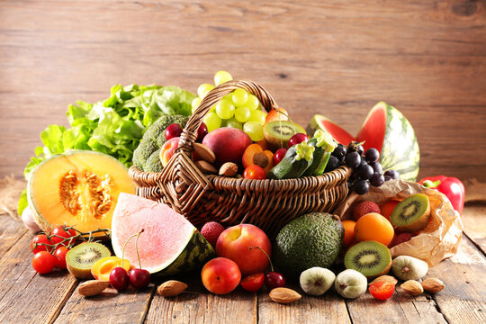 Abundant assortment of fresh fruits and vegetables in wicker basket on wood