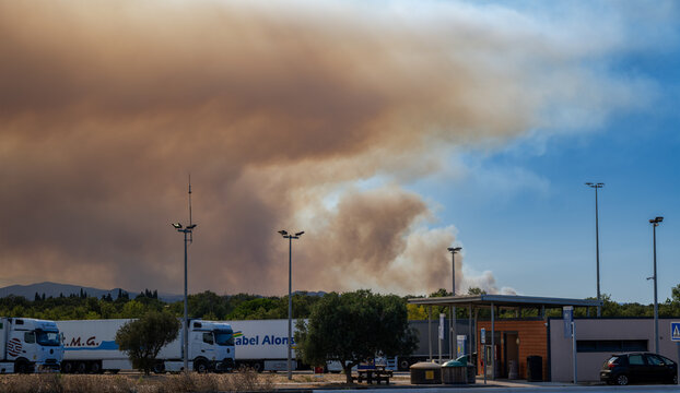 Pyr&eacute;n&eacute;es-Orientales, France, July 5, 2026: Smoke from the Tr&eacute;villach wildfire rises behind a highway service area and transport trucks near Perpignan during a major wildfire in southern France.