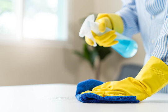 Close up of housekeeper in yellow gloves wiping table with microfiber cloth.