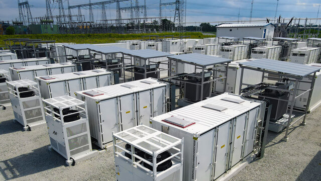 Battery energy storage system containers are charging at a large scale facility, connecting to a high voltage electrical substation in the background, supporting grid modernization