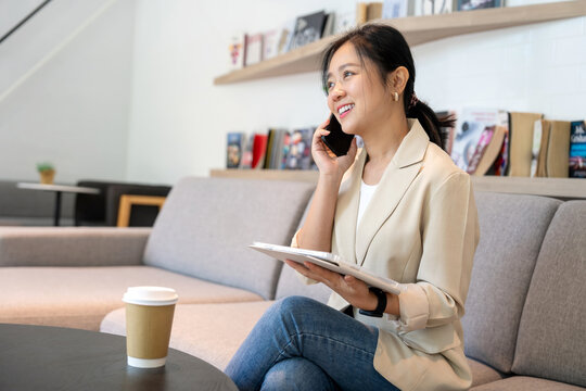Asian businesswoman uses a smartphone and laptop while sitting at a table in an outdoor city cafe.