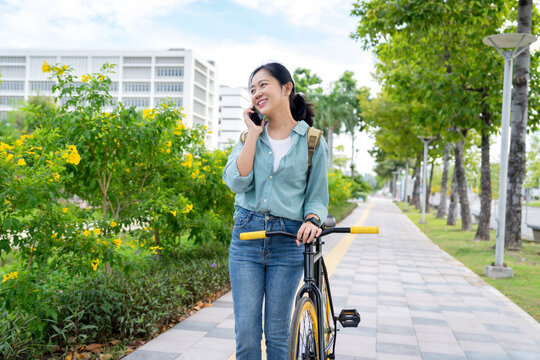 Asian woman happily walks and cycles to work in the city. She smiles while using her cell phone.