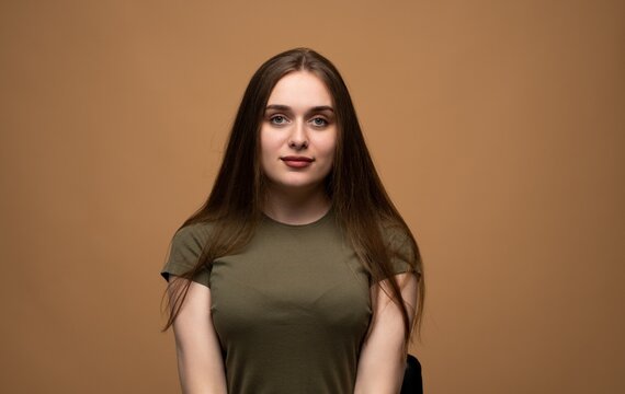 Young woman posing for portrait, showing calmness and confidence with soft smile on beige studio background