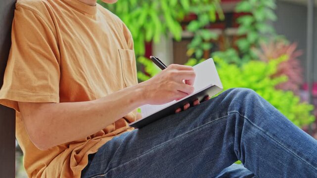 Close up of man sitting outside and writing notes in small book or planner