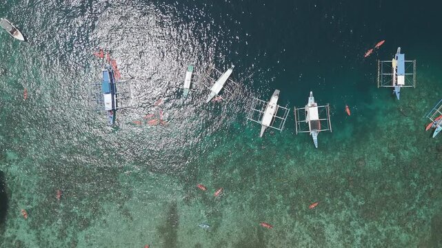 Top down drone view of bangka boats and swimmers over clear reef water