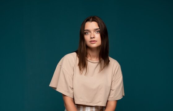 Young brunette woman posing in studio, wearing casual attire, looking directly at camera with natural expression