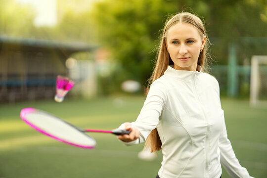 Confident female badminton player hitting a shuttlecock in mid-air on a sunny green court. Summer sport, precision, and golden hour action.