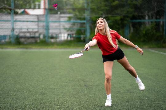 Young woman playing badminton on outdoor court. Active girl hitting shuttlecock with racket.
