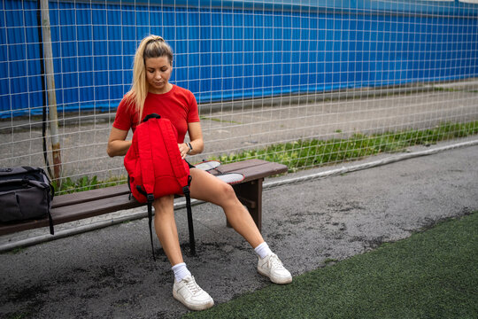 Young woman sitting on bench with backpack and badminton rackets laid out. Outdoor sports equipment and leisure activity ready.