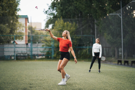 Woman watching her partner juggle shuttlecock with racket during badminton game. Observing sports skill and teamwork.