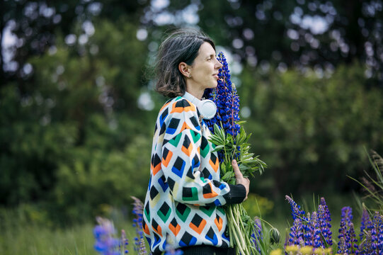 Woman holds lupine bouquet in summer field enjoying nature