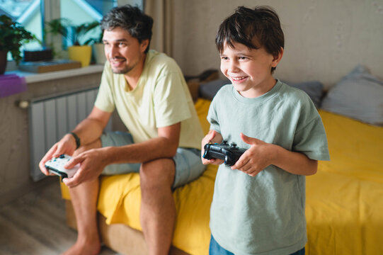 Father and son play video games together in the bedroom