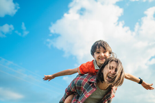 Happy mother gives her son a piggyback ride outdoors in summer