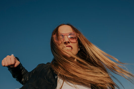 Portrait of aggressive young woman punching under blue sky