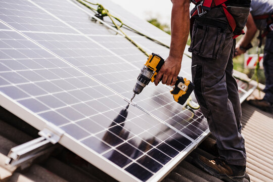 Electrician using power tool for installing solar panel on rooftop