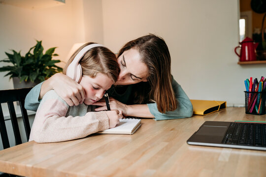 Mother kissing daughter doing homework at table at home