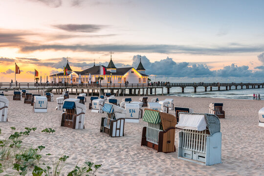 Germany, Mecklenburg-Vorpommern, Ahlbeck, Hooded beach chairs at sunset with pier and bathhouse in background
