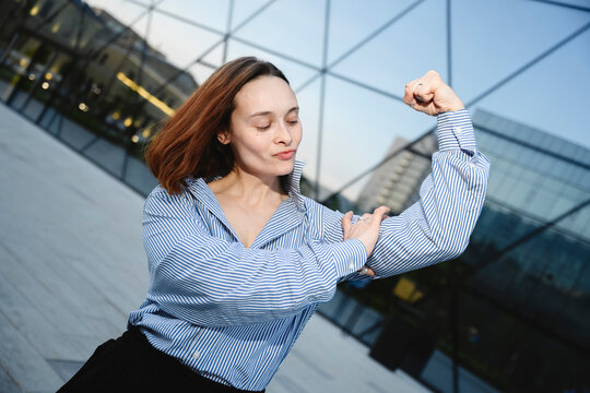 Confident businesswoman flexes her muscle outside a modern office