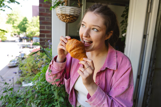 Happy woman eats a croissant on a tiny balcony in the morning