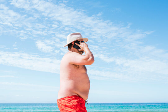 Mature overweight man talking on smart phone at beach during vacation