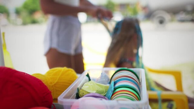 Many threads and ribbons lie on the table against the background of a girl whose African braids are weaving