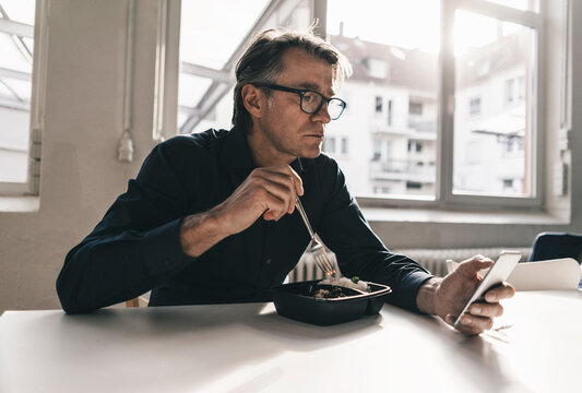Mature businessman checking cell phone during lunch break in office