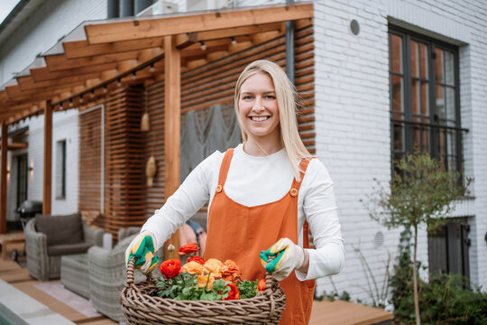 Smiling woman holding a basket of flowers while gardening outdoors