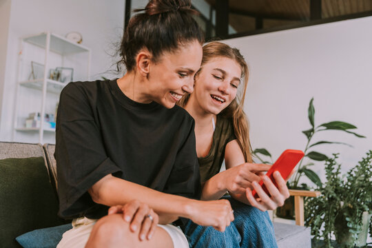 Smiling female friends looking at smart phone while sitting at home