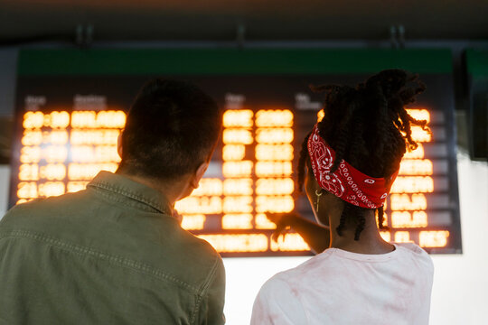 Multiracial friends checking time on departure board at railroad station