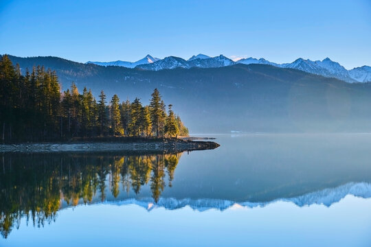 Snowcapped mountains reflected in calm lake, Lake Walchensee, Bavaria, Germany