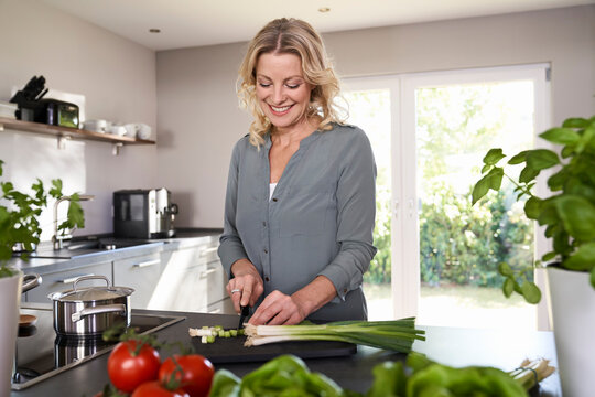 Smiling woman cutting spring onions in kitchen