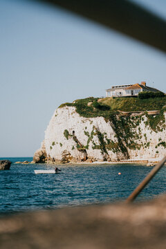 Coastal cliffside house overlooks blue ocean on a sunny summer day
