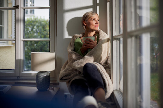 Smiling woman relaxes by the window at home with a warm beverage