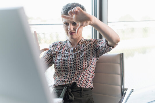 Businesswoman making finger frame while looking at computer in office