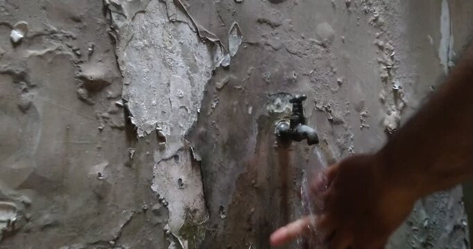 Washing hands under a dripping faucet on a textured wall.