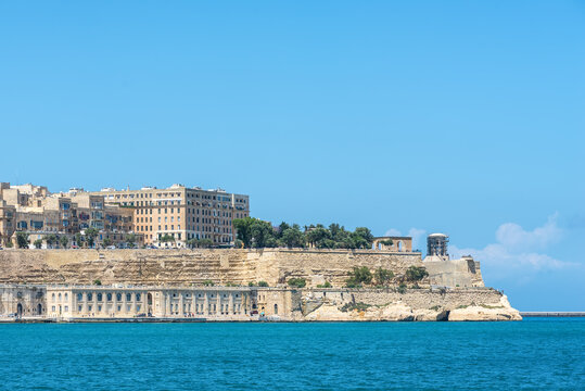 Panoramic view of Valletta, Malta, featuring historic limestone fortifications, the waterfront, and turquoise Mediterranean Sea under a clear blue sky. Iconic UNESCO heritage cityscape