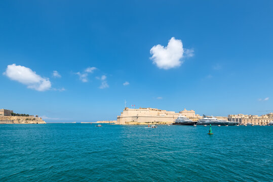 Wide‑angle view of Fort St. Angelo rising above Grand Harbour, with yachts on bright blue water and a clear sky overhead, capturing Malta&rsquo;s blend of historic fortifications and lively maritime scenery